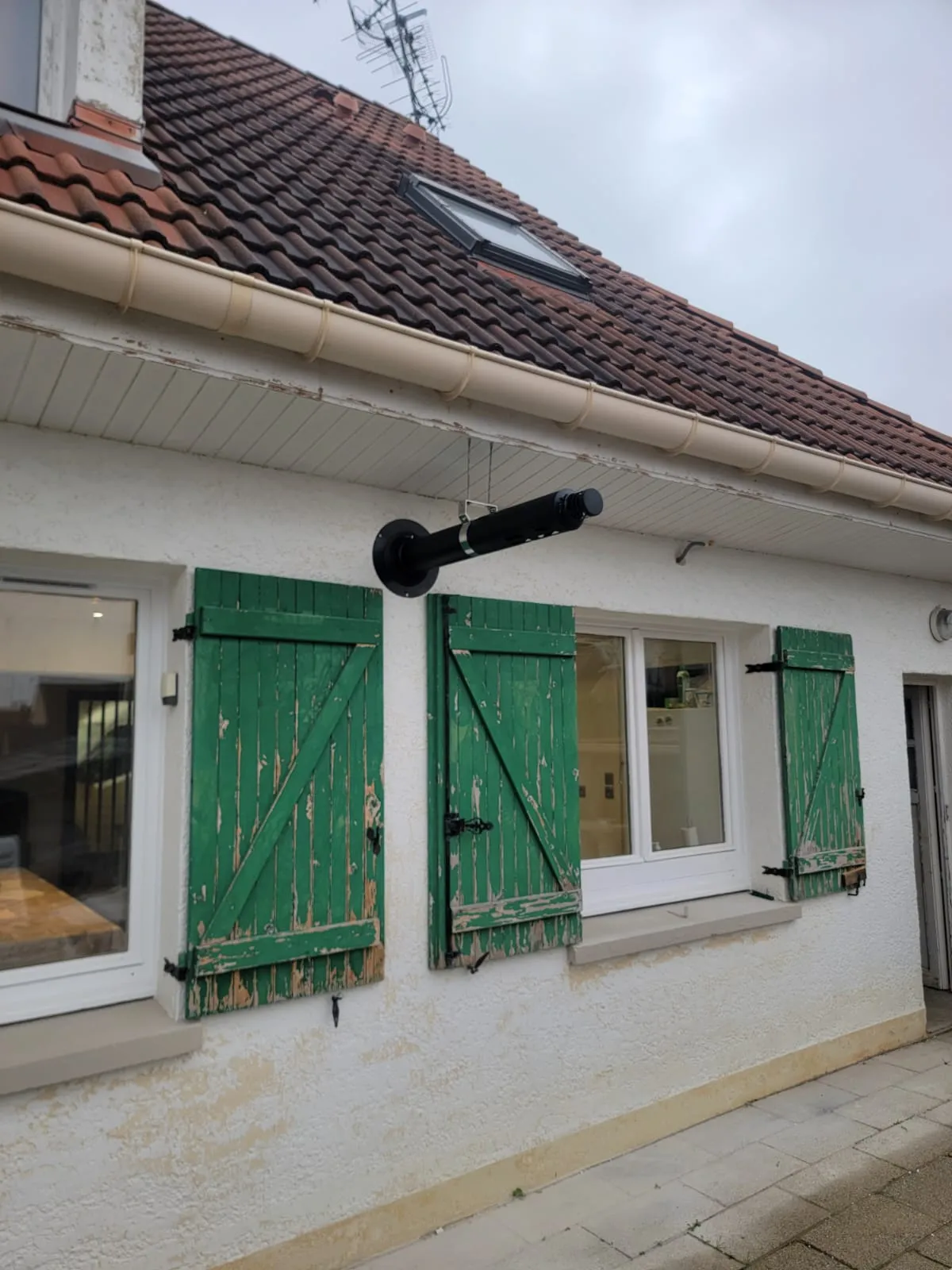 Conduit d'évacuation du poêle en sortie de façade, entre deux volets verts