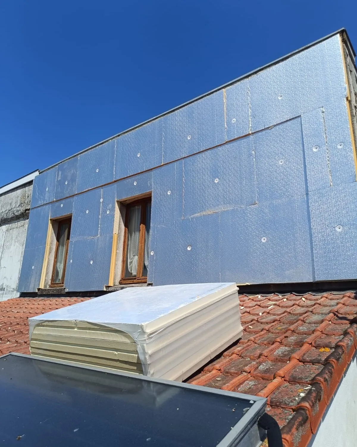 Panneaux isolants bleus posés sur la façade de la maison avant le bardage, à Barlin