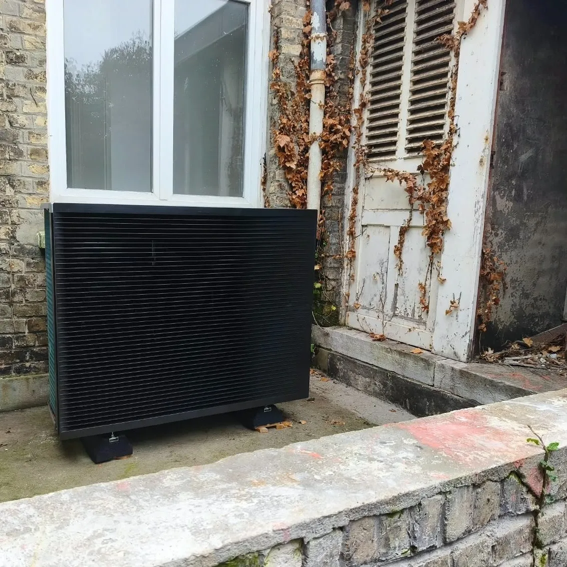 Unité extérieure noire de la pompe à chaleur Daikin haute température devant la façade, à Calais