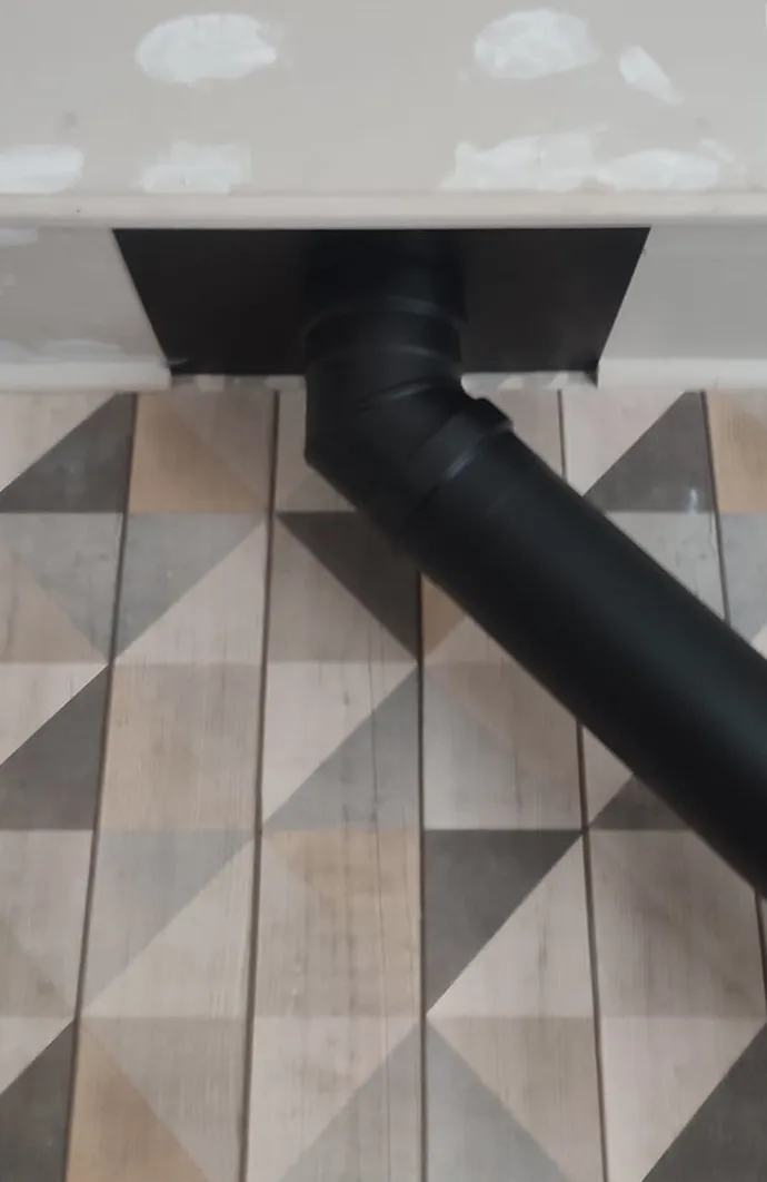 Conduit noir du poêle raccordé au mur, détail du carrelage