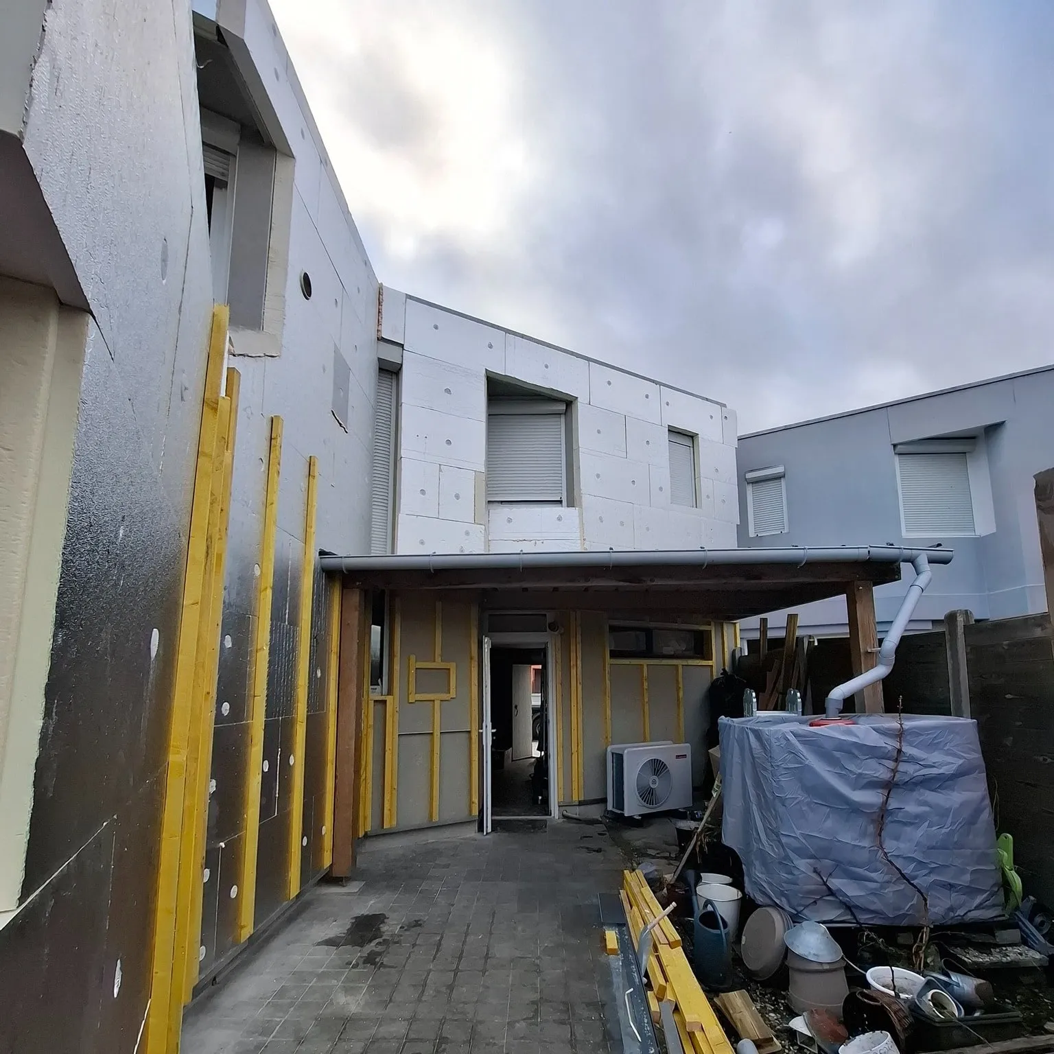 Ossature bois en cours de pose sur la maison, bardage blanc déjà posé sur une partie