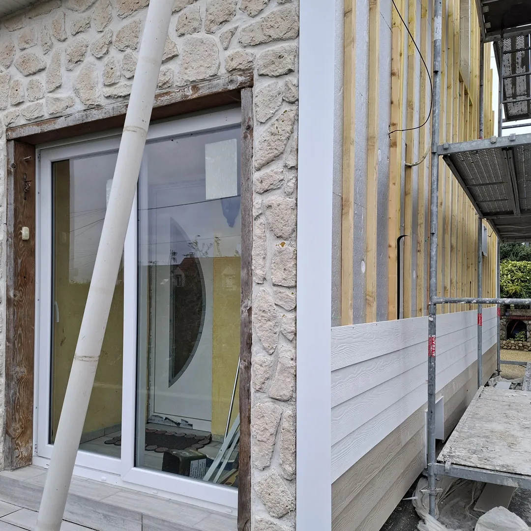 Façade en cours : mur en pierre d'un côté, bardage Cedral posé de l'autre, à Marquise