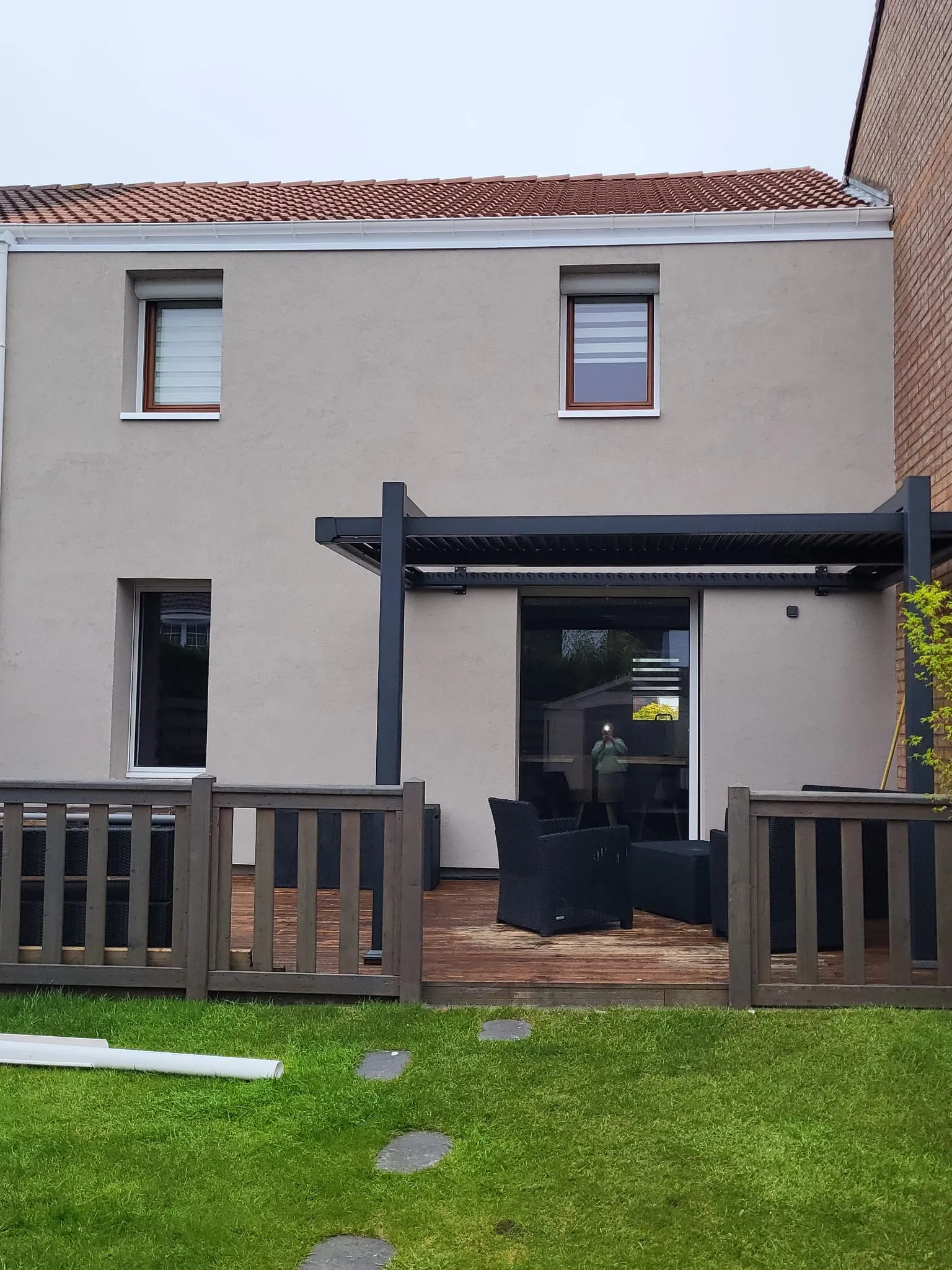 Façade arrière isolée par l'extérieur et enduite en gris clair, avec pergola et terrasse, à Saint-Léonard