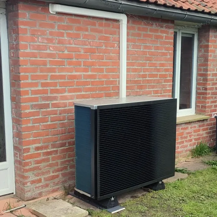 Unité extérieure de pompe à chaleur Daikin posée au sol contre un mur de briques, à Volckerinckhove