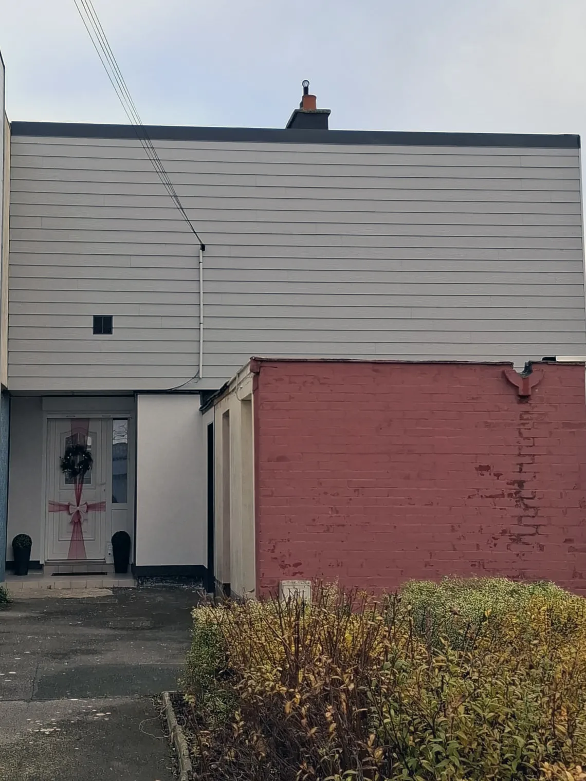 Entrée de la maison : bardage clair posé à côté d'un mur en briques rouges non traité